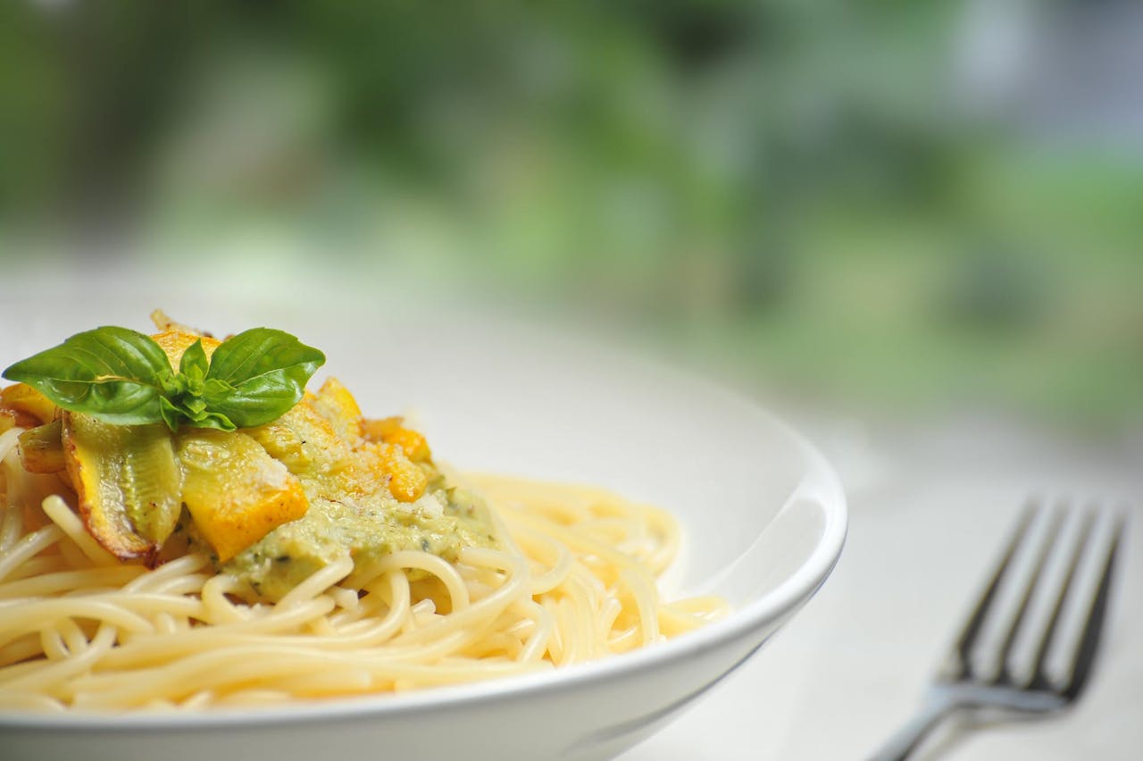 Close-up of freshly made spaghetti topped with basil and creamy pesto sauce in a white dish.